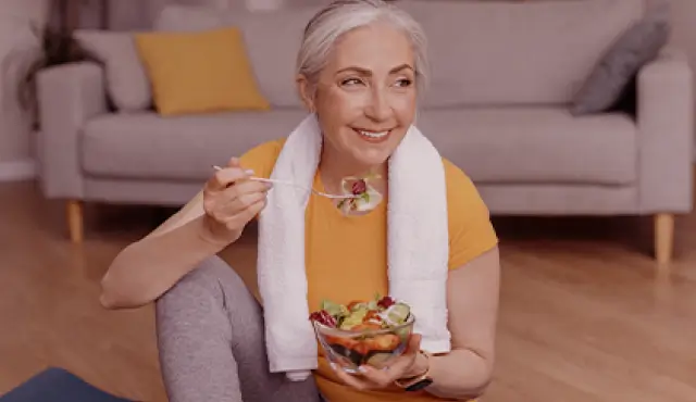 Mujer comiendo una ensalada sentada en el piso de la sala después de ejercitarse